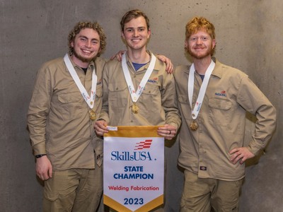 Three men wear gold medals and hold a championship banner.